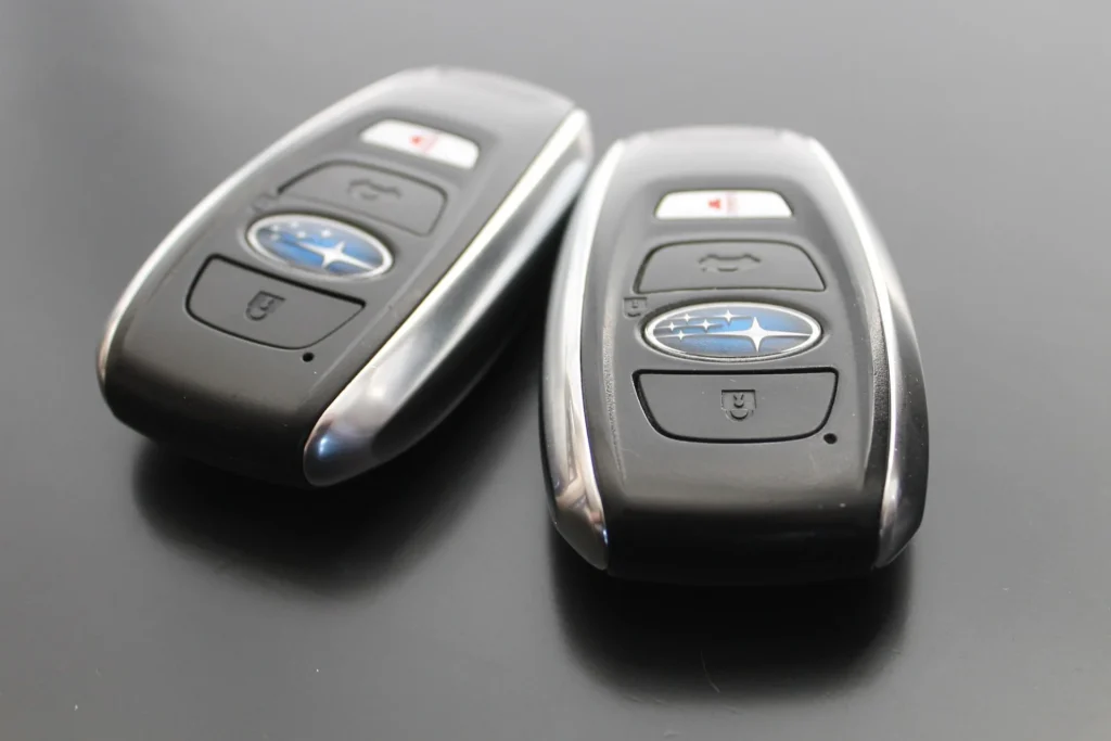 Two black Subaru key fobs with remote buttons on a black surface
